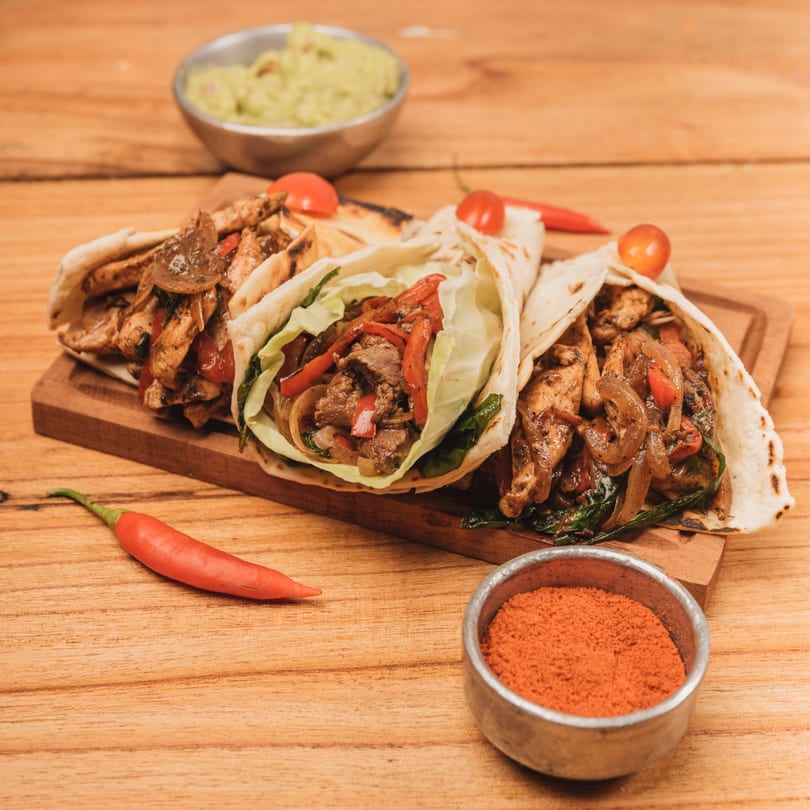 Three Rose's Mexican Restaurant fajita wraps, with guacamole and chili powder, on a wooden board.