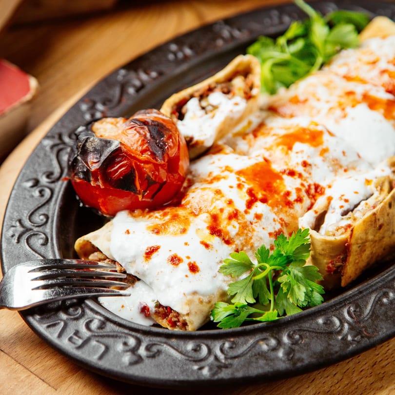 Rose's Mexican Restaurant enchiladas topped with white sauce, red drizzle, and a charred tomato.